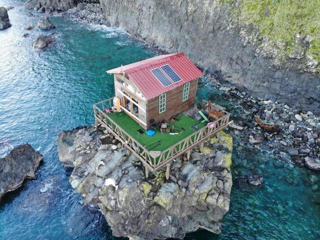 Deniz kıyısındaki kayanın üzerine yapılan baraka dikkat çekiyor