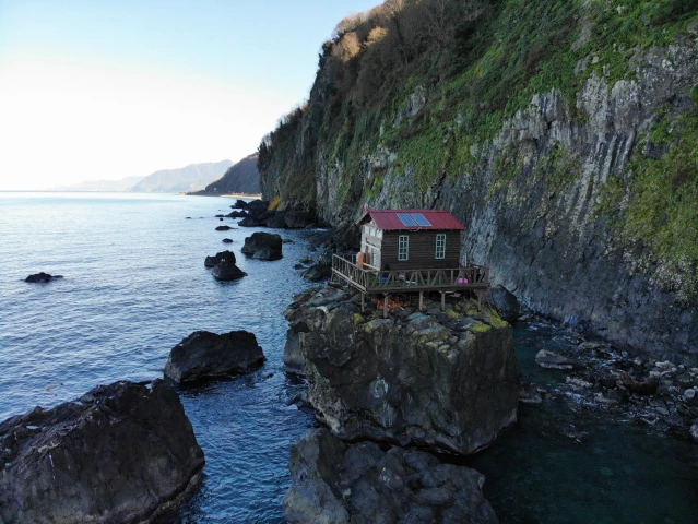 Deniz kıyısındaki kayanın üzerine yapılan baraka dikkat çekiyor